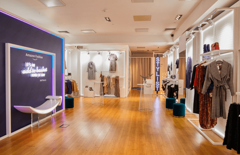 Amazon Fashion showroom with clothing racks and a neon sign reading 'It's an add to basket kind of day